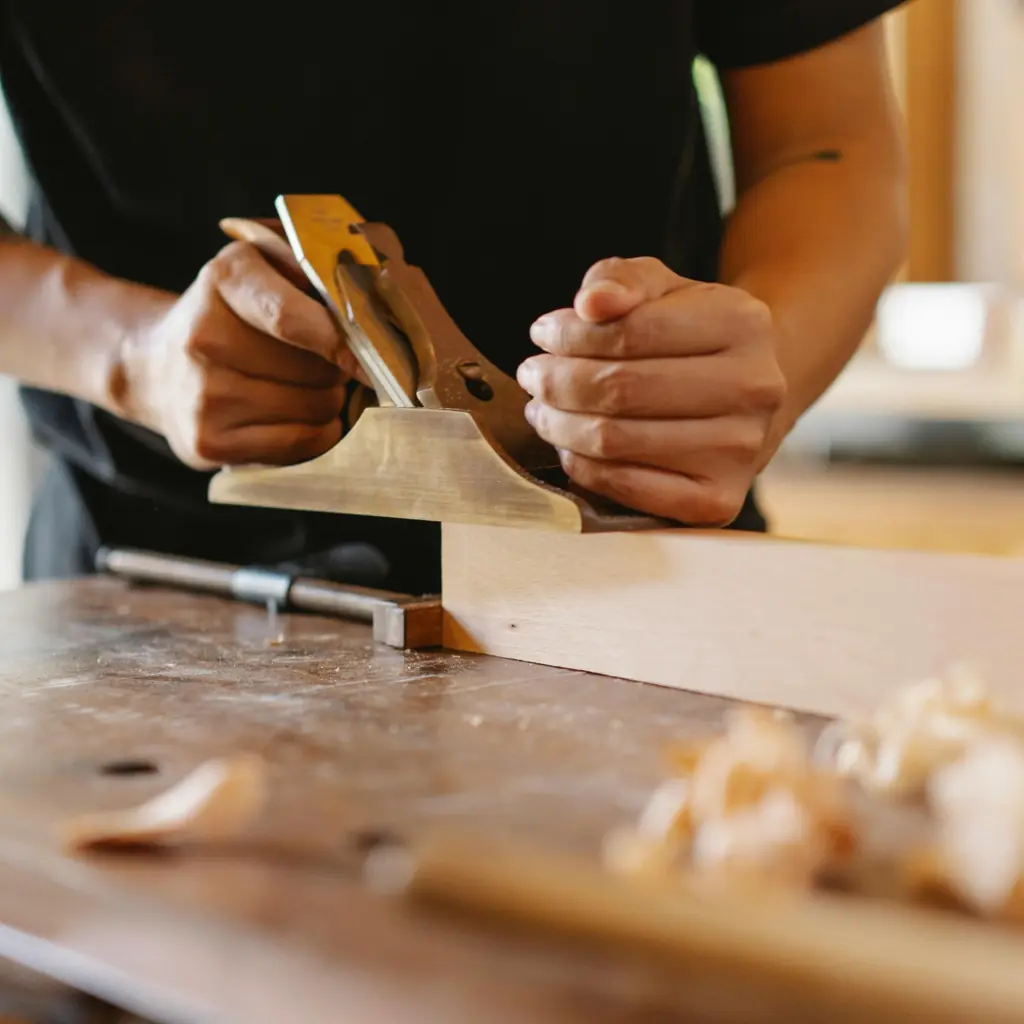 Craftsperson using a hand plane to shape wood, representing dedication to quality craftsmanship and attention to detail
