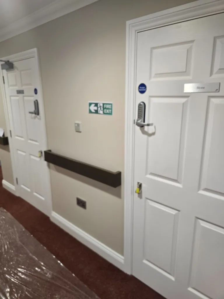 White panel doors in corridor with keypad lock, fire exit sign and wall protection rail
