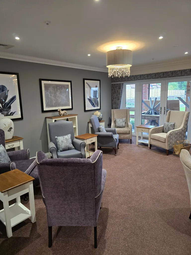 Lounge seating area with upholstered armchairs, side tables, wall artwork and chandelier lighting by patio doors