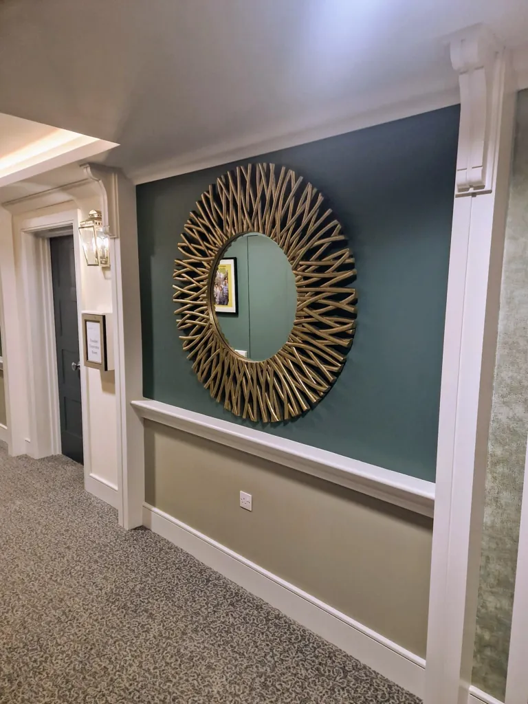 Decorative corridor wall with large circular sunburst mirror, panelled wainscoting and carpet flooring