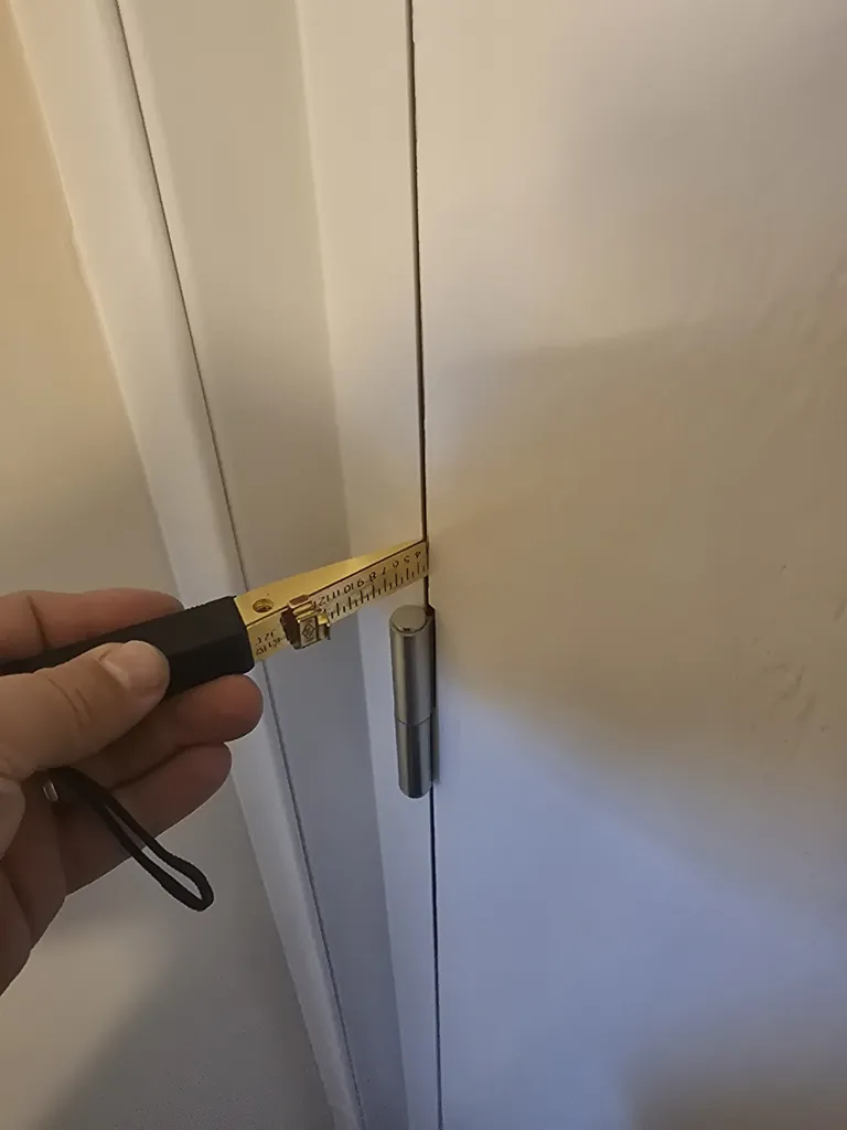 Close-up of door hinge with measuring tool checking gap between door leaf and frame