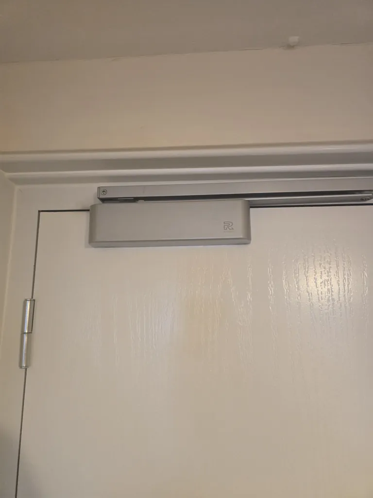 Overhead door closer installed on white door with track mechanism fixed to frame