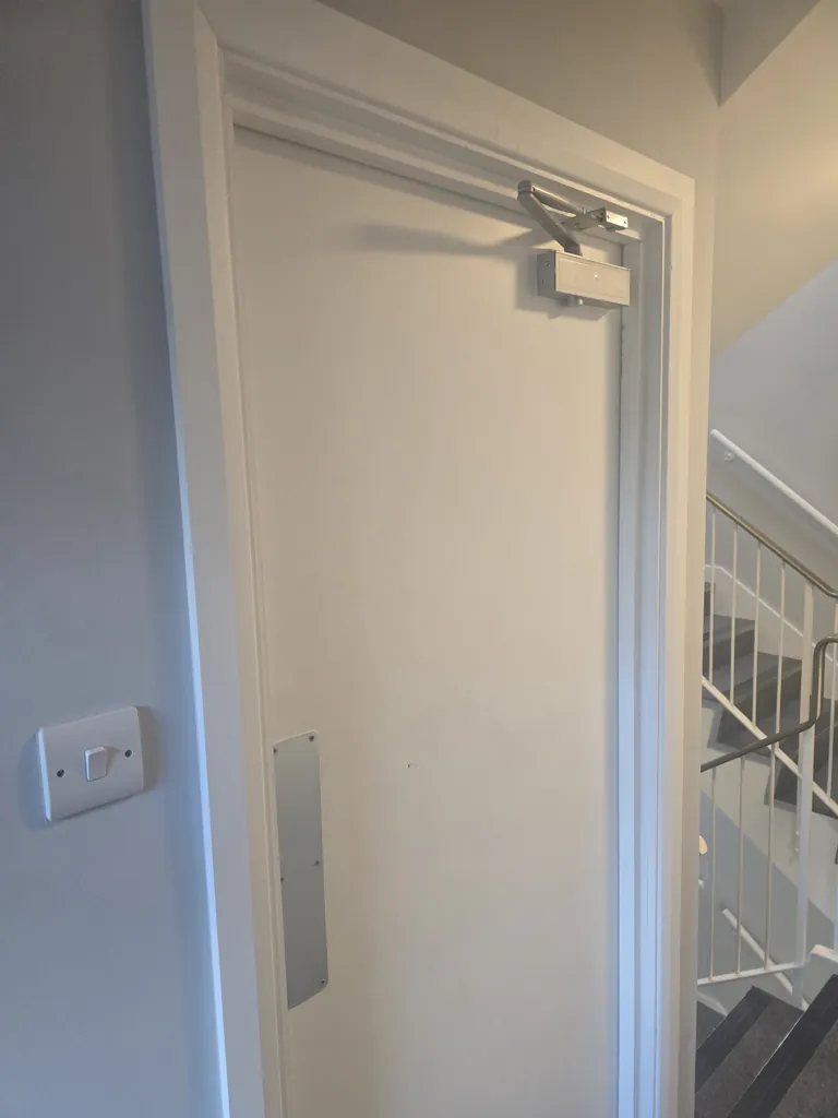 White fire door with overhead closer and metal push plate in stairwell corridor
