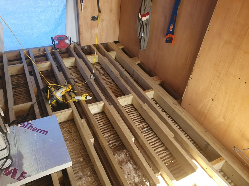 Loft floor under construction with exposed timber joists, insulation and tools during installation