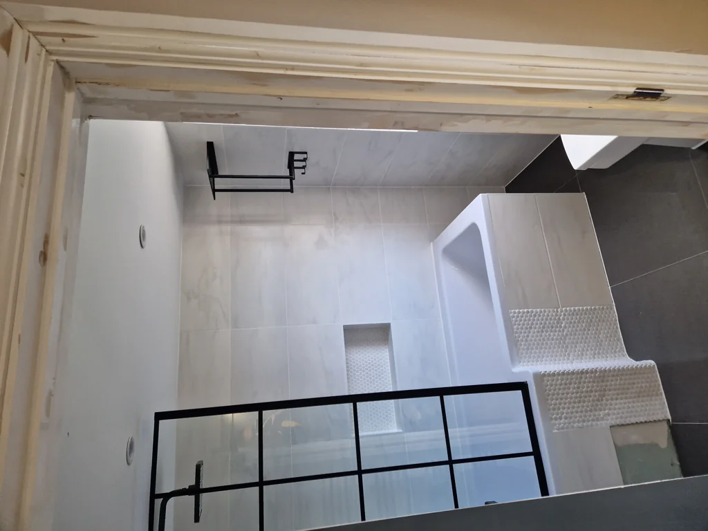 Bathroom installation in progress with tiled walls, shower enclosure frame and bathtub visible from above